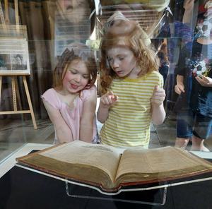 The First Folio on display. The book is open so that you can see two pages. Two young girls are looking at the book.