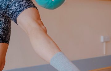 A close up of a leg and arm doing pilates with a ball.