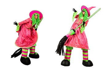 Two people on stilts, dressed in bright pink and green witch costumes with brooms.