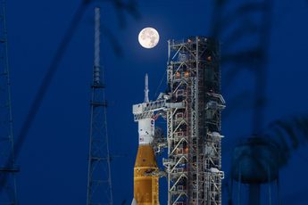 A rocket on launchpad with moon behind it.