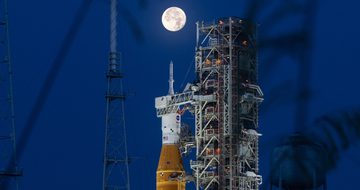 A rocket on launchpad with moon behind it.