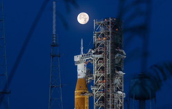 A rocket on launchpad with moon behind it.