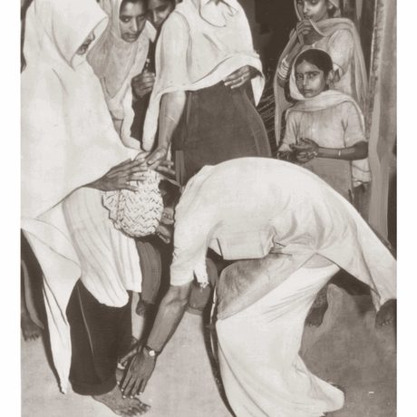Black and white photo of a person kneeling at someone's feet.