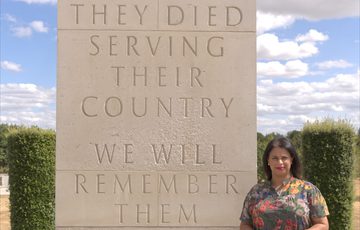 A person standing in front of a large stone memorial that reads "They died serving their country. We will remember them."