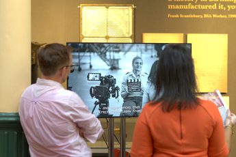 Two people standing in front of TV screen in a gallery.