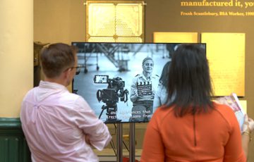 Two people standing in front of TV screen in a gallery.