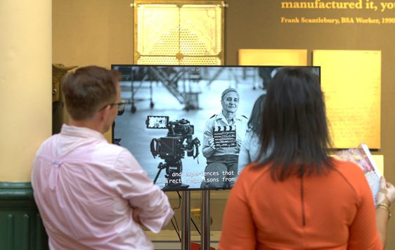 Two people standing in front of TV screen in a gallery.
