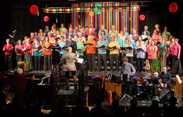 A group of people wearing colourful tops singing in a choir on stage.