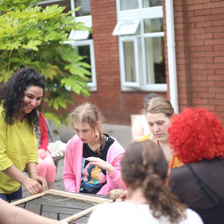 A person standing while a group of people are seated at a table a doing a craft activity.