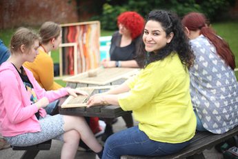 A group of people who are seated at a table the artist is looking to the camera and smiling.