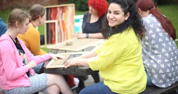 A group of people who are seated at a table the artist is looking to the camera and smiling.