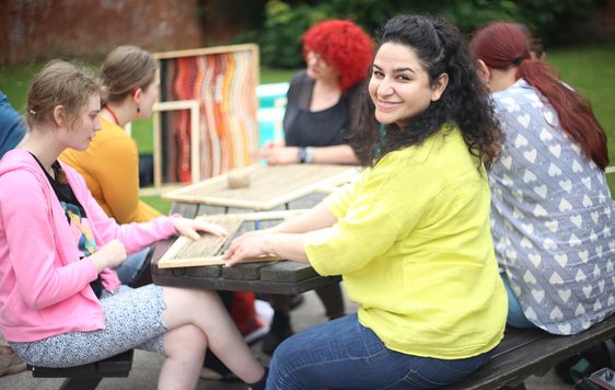 A group of people who are seated at a table the artist is looking to the camera and smiling.