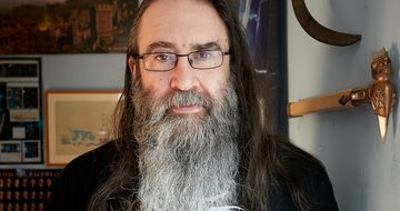 A portrait photo of a man with long hair and beard wearing a black t-shirt.