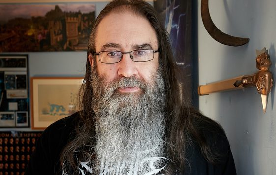A portrait photo of a man with long hair and beard wearing a black t-shirt.