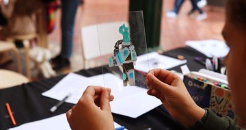 A child holding a drawing of a creature on a clear perspex sheet.