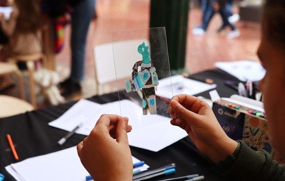 A child holding a drawing of a creature on a clear perspex sheet.
