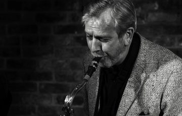 A black and white portrait of a person playing the saxophone.