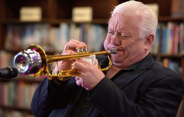 A person playing a trumpet in a library setting.