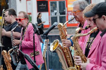 A group of people playing a selection of brass instruments and performing in a street scene.