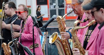 A group of people playing a selection of brass instruments and performing in a street scene.