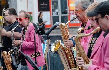 A group of people playing a selection of brass instruments and performing in a street scene.