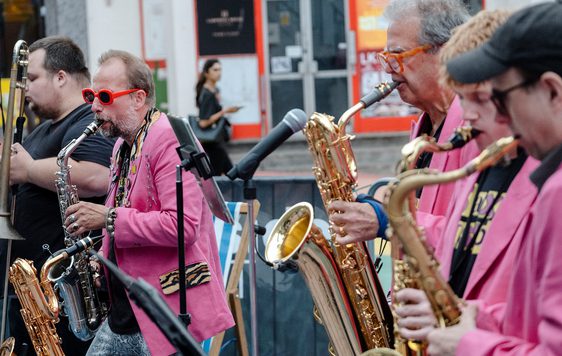 A group of people playing a selection of brass instruments and performing in a street scene.