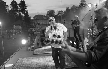 A black and white photo of a band on stage with a person singing in the centre.