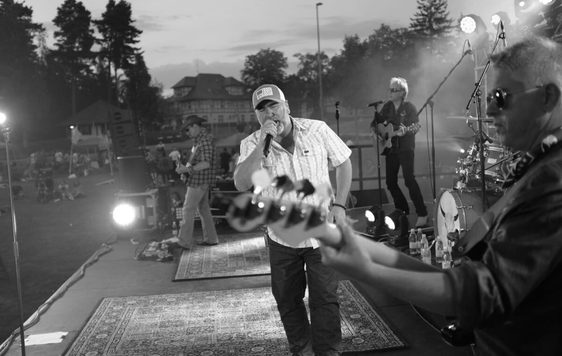A black and white photo of a band on stage with a person singing in the centre.