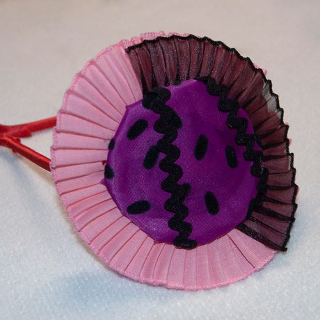 A craft item of a purple fabric circle surrounded by a folded pink ribbon edge.