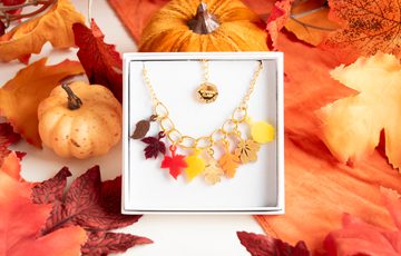 A colourful necklace designed with leaves in a box surrounded by decorative leaves and pumpkins.