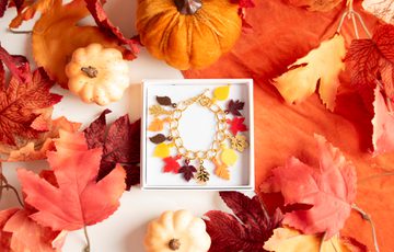 A colourful bracelet designed with leaves in a box surrounded by decorative leaves and pumpkins.