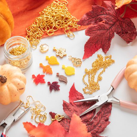 Autumnal jewellery making materials and tools surrounded by decorative leaves and pumpkins.