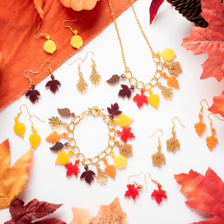 A selection of necklaces, earrings and bracelets designed with colourful autumnal leaves, surrounded by decorative leaves and pumpkins.