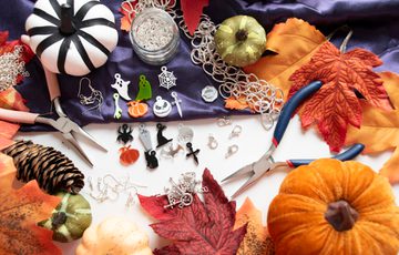 Autumnal and halloween themed jewellery making materials and tools surrounded by decorative leaves and pumpkins.