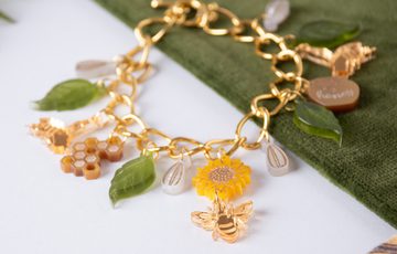 Close up of a gold bracelet with leaf, sunflower and bee design, laid out on display.