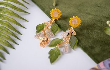 Close up of set of earrings with sunflowers, leaf and bee design.
