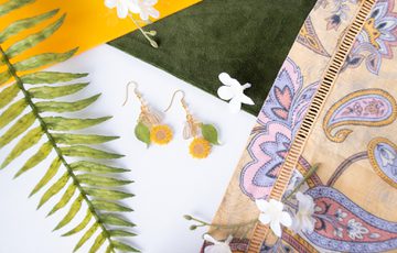 Close up of a set of earrings with sunflowers and leaf design.