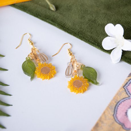 Close up of set of earrings with sunflower and leaf design.