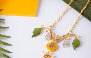 A necklace designed with leaves at the either end, and a sunflower and bee in the centre.