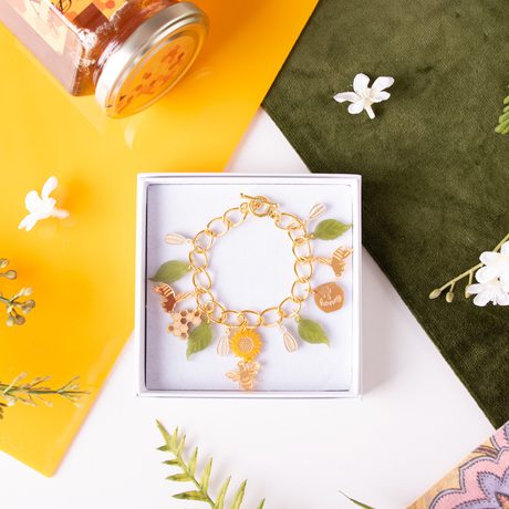 A bracelet designed with leaves, sunflowers and bees in a box, surrounded by fabric, leaves and a honey pot.