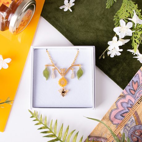 A neclace designed with leaves, sunflowers and bees in a box, surrounded by fabric, leaves and a honey pot.