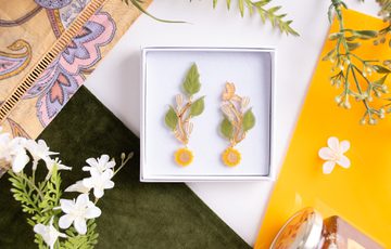 Earring designed with leaves, sunflowers and bees in a box, surrounded by fabric, leaves and a honey pot.