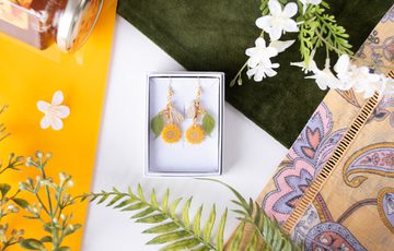 Earring designed with leaves, sunflowers and bees in a box, surrounded by fabric, leaves and a honey pot.