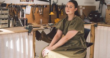 A person smiling sitting in a jewellery making workshop.