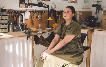 A person smiling sitting in a jewellery making workshop.