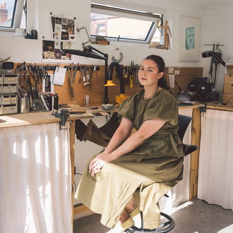A person smiling sitting in a jewellery making workshop.
