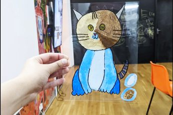 Hand holding perspex sheet with illustration of a cat on it.