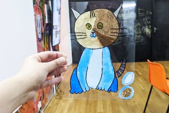 Hand holding perspex sheet with illustration of a cat on it.