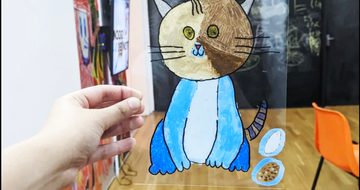 Hand holding perspex sheet with illustration of a cat on it.