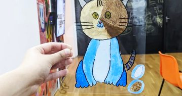 Hand holding perspex sheet with illustration of a cat on it.